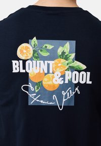 Mørkeblå t-shirt med et grafisk print af appelsiner og blade samt teksten "BLOUDT & POOL" og "California Valley" i hvid skrift.