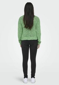 Zielony sweter z dzianiny o fakturowanym wzorze, dopasowanym kroju i ściągaczu u dołu, zestawiony z ciemnymi, obcisłymi jeansami i białymi trampkami.