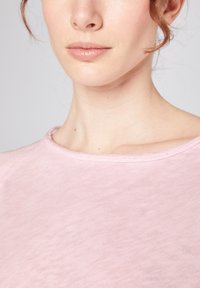 Helles pinkes T-Shirt mit Rundhalsausschnitt, weichem Material und einem einfachen, gesteppten Saum, das sich auf minimalistisches Design und Komfort konzentriert.