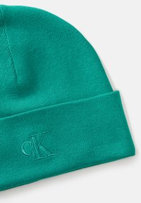 Teal knit beanie made of stretchy fabric. Features a folded cuff and embroidered "cK" logo on the front. Smooth texture, no patterns.