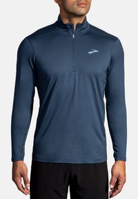 Marineblaues Langarm-Sportshirt mit Viertel-Reißverschluss-Kragen, schmalem Schnitt, glatter Textur, reflektierendem Logo auf der Brust und Flatlock-Nähten.
