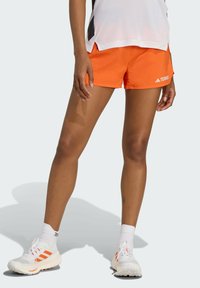 Oranžové atletické šortky so bočnými vreckami, ktoré majú biele logo "TERREX" a kontrastné čierne akcenty na ľahkej látke.