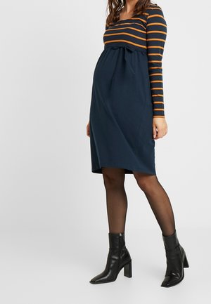 Sukienka ciążowa z granatowym gorsetem i pomarańczowymi poziomymi paskami. Posiada marszczoną talię z kokardą. Czarne botki do kostek dopełniają stylizację.