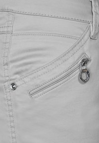 Jasnoszare dżinsy z materiału z zamkiem błyskawicznym w kieszeni. Cechy to srebrny zamek, okrągły akcent wykorzystujący metal i szczegółowe szwy.