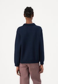 Temno modra pletena pulover s visokim ovratnikom, žabastimi rokavi in robom. Ima sproščen kroj in je nosil z svetlo roza hlačami.