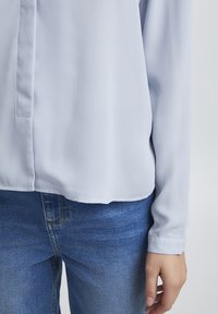 Blusa azzurro chiaro con una trama liscia, caratterizzata da una linea dritta e maniche lunghe. Abbinata a jeans in denim blu classico.