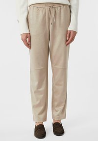 Beige, lässige Hose mit elastischem Bund und Kordelzug. Glattes Material mit Nahtakzenten. Kombiniert mit dunkelbraunen Slippern.