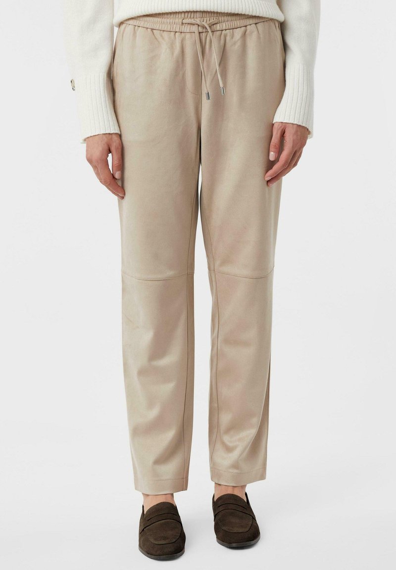 Beige, lässige Hose mit elastischem Bund und Kordelzug. Glattes Material mit Nahtakzenten. Kombiniert mit dunkelbraunen Slippern.