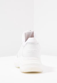 Zapatilla deportiva blanca con parte superior de cuero suave, cuello acolchado y suela blanca texturizada. Logo en relieve "BRONX" en el talón.