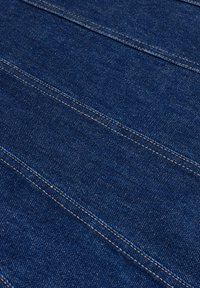 Tkanina dżinsowa w ciemnoniebieskim odcieniu z ukośnymi liniami szwów. Tekstura jest gładka, z widocznymi wzorami splotu i kontrastującą złotą nicią.