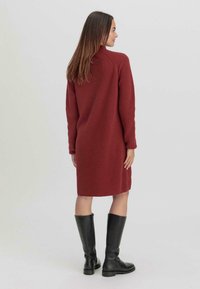Abito maglione a coste color marrone con maniche lunghe, orlo di lunghezza media e colletto alto, abbinato a stivali neri fin sopra il ginocchio.