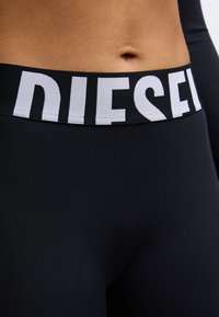 Czarne legginsy z szerokim czarnym pasem w talii ozdobionym białym napisem "DIESEL". Materiał gładki i dopasowany do sylwetki.
