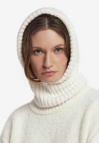 Biały sweter o grubym splocie z wysokim prążkowanym golfem i kapturem. Przytulna faktura z lekko nierównym wzorem na całej powierzchni.