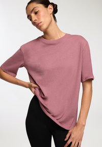 Różowa bawełniana koszulka z luźnym fasonem, krótkimi rękawami i okrągłym dekoltem, w zestawie z czarnymi legginsami; gładka tekstura z minimalnymi detalami.