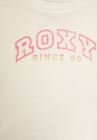 Hvit hettegenser med "ROXY" i rosa og grønn blokkbokstaver. Har rund hals og myk stoff med minimal tekstur.