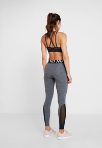 Soutien-gorge de sport noir avec des bretelles croisées, associé à un legging gris avec des panneaux transparents et une ceinture de marque. Des baskets légères viennent parfaire le look.