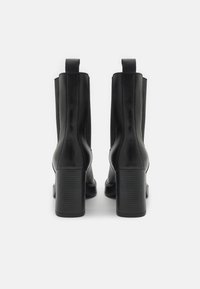 Černé kožené kotníkové boty s masivním podpatkem, se strečovými bočními panely a poutky pro snadné obouvání. Hladký povrch a minimalistický design.