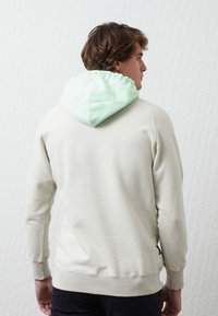Sudadera gris claro con capucha verde menta. Presenta un corte relajado, puños y dobladillo acanalados, y una etiqueta de logo en la parte posterior. Textura de tela suave.