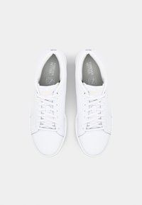 Une paire de baskets blanches Puma avec des lacets, vue d'en haut sur un fond gris clair uni.