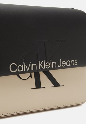 Cartera Calvin Klein Jeans en negro y beige con gran logo CK en relieve y nombre de la marca impreso en la solapa frontal.