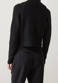 Černý zkrácený svetr s ribbed límcem a lemem, vyrobený z texturované tkaniny, spárovaný s černými kalhotami s elegantními zadními kapsami.