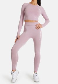 Vaaleanpunainen pitkähiha croptop ja siihen sopivat korkeavyötäröiset legginssit joustavasta kankaasta. Legginseissä on valkoinen "squatproof" -teksti.