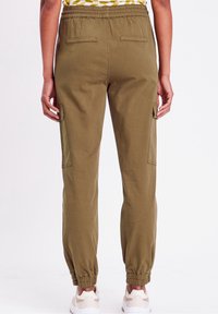 Pantalon de jogging vert olive avec une taille élastique, deux poches arrière, et des poches cargo latérales ; chevilles retroussées ; porté avec des baskets blanches.