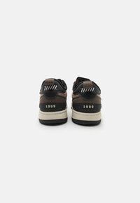 Černé a hnědé tenisky s texturovaným svrškem, bílými akcenty a rokem "1999" výrazně vyraženým na patě.