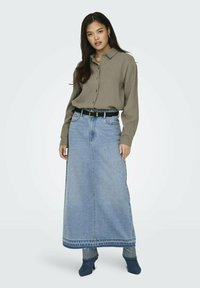 Grüne Hemdbluse, denim Maxi-Rock, schwarzer Gürtel und blaue Absätze. Der Rock hat einen fransigen Saum und eine lockere Passform. Strukturiertes Material.