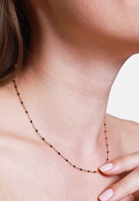 Goldkette mit gleichmäßig verteilten schwarzen Perlen. Zartes Design mit einer einfachen, glatten Textur. Wird auf nackter Haut getragen.