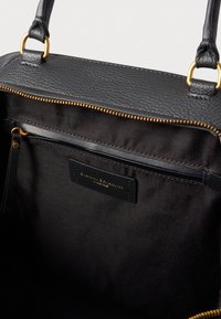 Mustan nahkalaukun sisäosa, jossa on kultainen vetoketju, kangasvuori ja pieni tasku, jossa on merkki. Sileä pinta ja jämäkkä muotoilu.