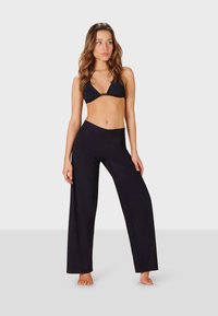 Svart bikiniöverdel med triangelformade kupor och en guldfärgad detalj. Svarta vida byxor i slätt tyg, åtsittande vid midjan och ankellånga.