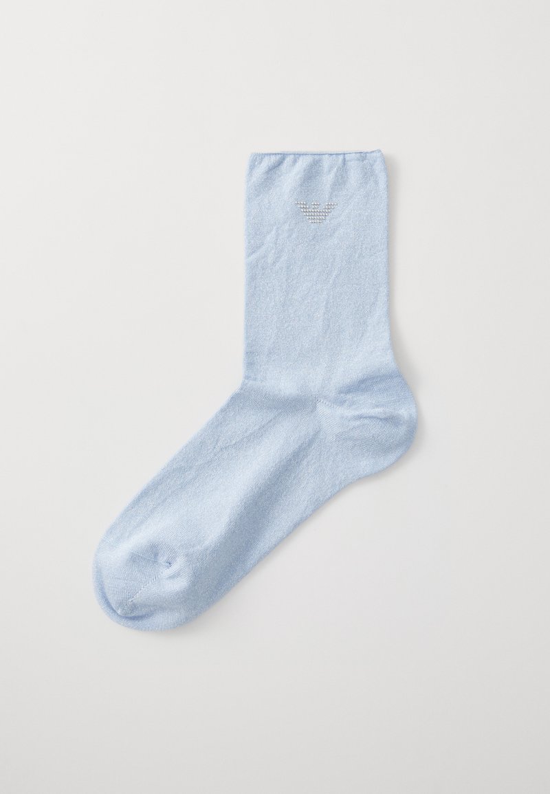 Ljusblå strumpa gjord av mjukt tyg, med en subtil lyster och en liten, strukturerad logotyp nära toppen. Standard strumpform med en rundad tå.