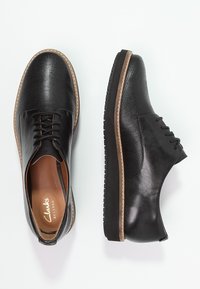 Chaussures en cuir noir avec surface texturée, design à lacets, semelle extérieure contrastante couleur tan et finition lisse. Présentent un marquage discret sur la semelle intérieure.