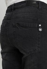 Černé džíny z denimu se zvýšeným pasem, dvěma zadními kapsami se švy ve tvaru vlny a detaily s logem na kovových prvcích.