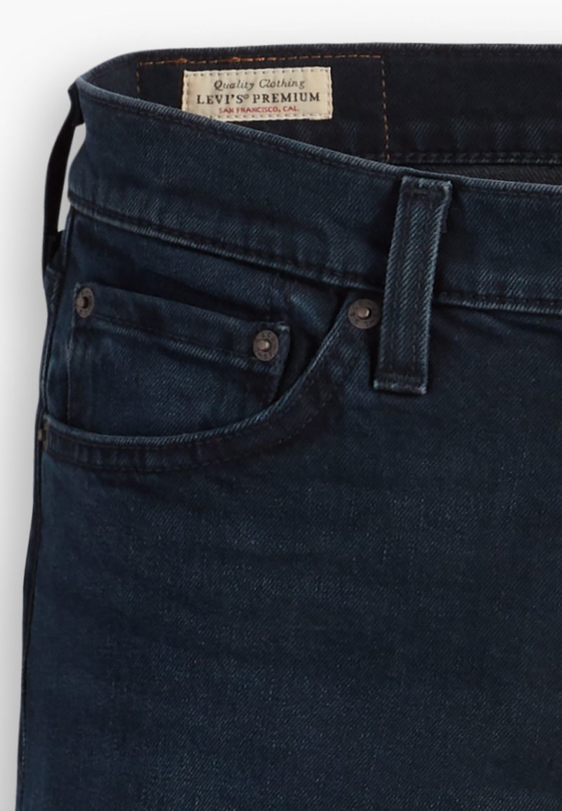 Vaqueros de mezclilla azul oscuro con un diseño liso, estilo de cinco bolsillos, herrajes metálicos para el cierre y la etiqueta Levi's Premium en la cinturilla.