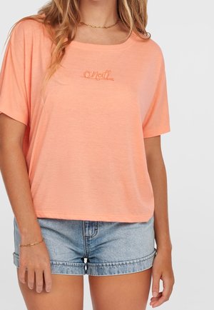 Woman wearing a loose peach-colored O'Neill t-shirt and light blue denim shorts, with a gold chain necklace and bracelet.