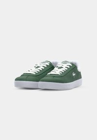 Green suede sneakers feature white laces, a padded collar, and a white rubber sole. Branding appears on the tongue and side.