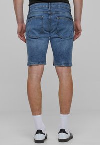 Shorts en denim bleu clair avec une coupe classique, dotés de poches arrière et d'un détail en chaîne. Coupés juste au-dessus du genou avec une texture lisse.