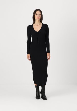 Black ribbed knit dress with long sleeves, V-neck, and drawstring detail at the front. Fitted silhouette extends to mid-calf.