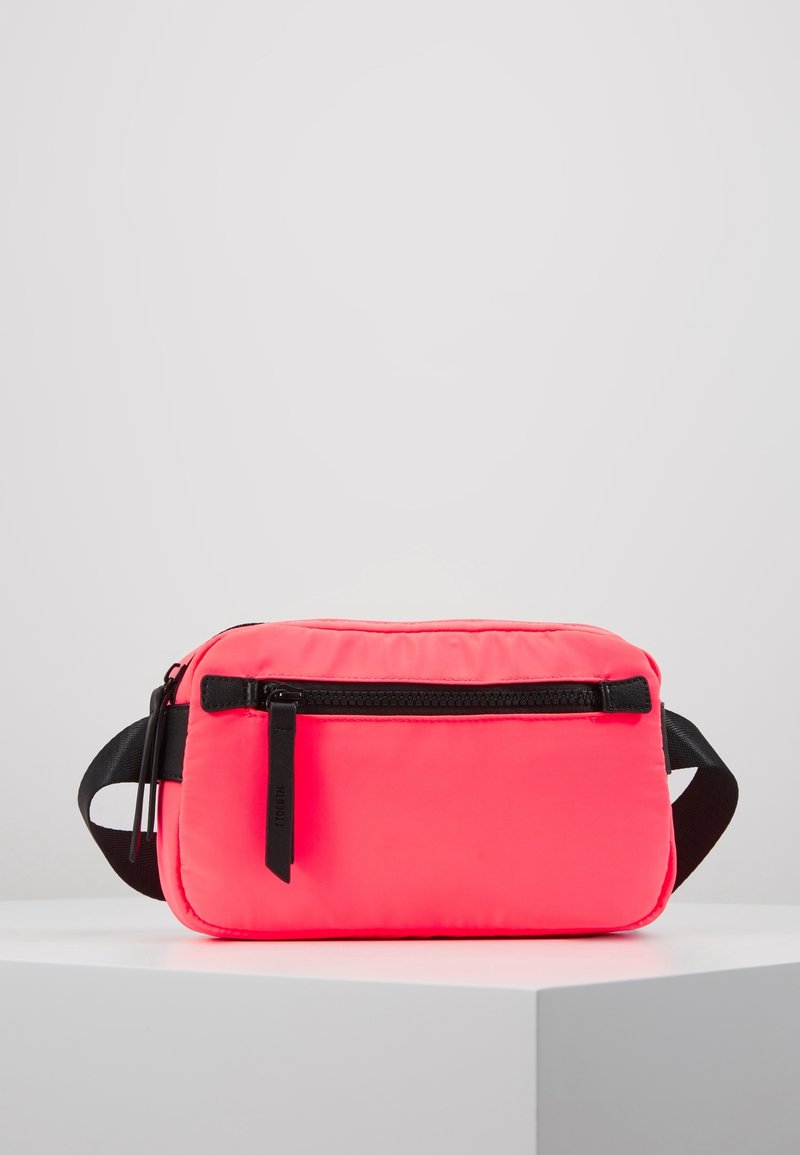 Sac banane rectangulaire rose vif avec fermeture éclair noire et sangle noire ajustable, présenté sur un socle blanc sur fond gris clair.