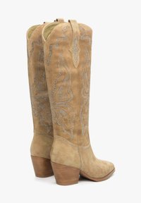 Brązowe zamszowe kowbojki z motywem w kształcie motyla ozdobione srebrnymi ćwiekami, z wydłużonym noskiem i podwyższoną piętą.