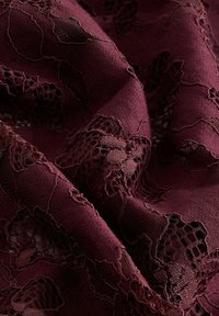 Burgunderrødt stof med detaljerede blonder, herunder blomsterprint og varierede teksturer, der fremhæver transparens og dybde.