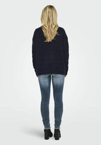 Tengerész kék kötött pulóver laza szabással és bordázott mandzsettákkal, elhalványult slim fit farmernadrággal és fekete tömör sarkú bokacsizmával párosítva.