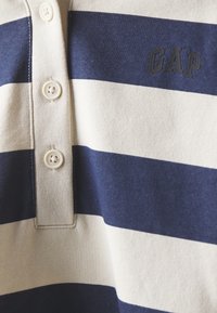 Polokošile s námořnicky modrými a krémovými vodorovnými pruhy, se třemi knoflíky u límce, s černým logem "GAP" na hrudi.