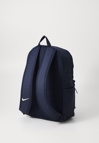 Tamsiai mėlyna kuprinė, pagaminta iš patvarios medžiagos, su paminkšlintomis petnešėlėmis, priekine kišene ir balto logotipo akcentu.