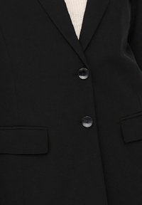 Černý blazer z hladkého materiálu s dvěma knoflíky, klopovými límci a bočními kapsami. Viditelný strukturovaný světle béžový interiér.