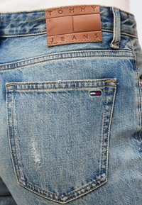 Τσέπη πίσω από τζιν ελαφριάς μπλε denim με μικρή σημαία Tommy Hilfiger και καφέ δερμάτινη ετικέτα στη μέση που γράφει "Tommy Jeans".