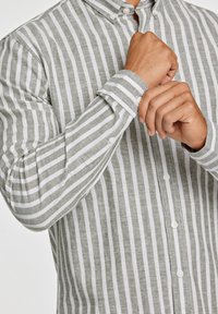 Lys grøn og hvid stribet button-up skjorte lavet af linned. Har en krave, lange ærmer og hvide knapper foran.