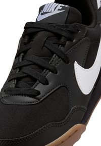 Zapatilla Nike negra con un upper de cuero y tela texturizada, logo blanco, costuras intrincadas y cordones negros sobre una suela de goma.